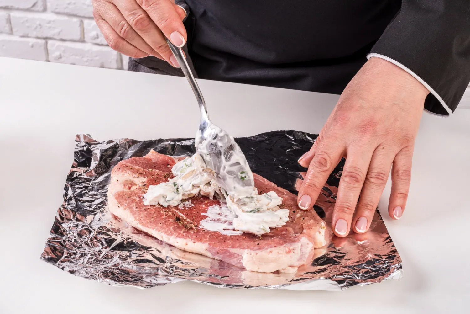 Mano aplicando una mezcla cremosa sobre un filete de carne en papel aluminio, destacando una técnica de cocina para preparar un platillo sabroso.